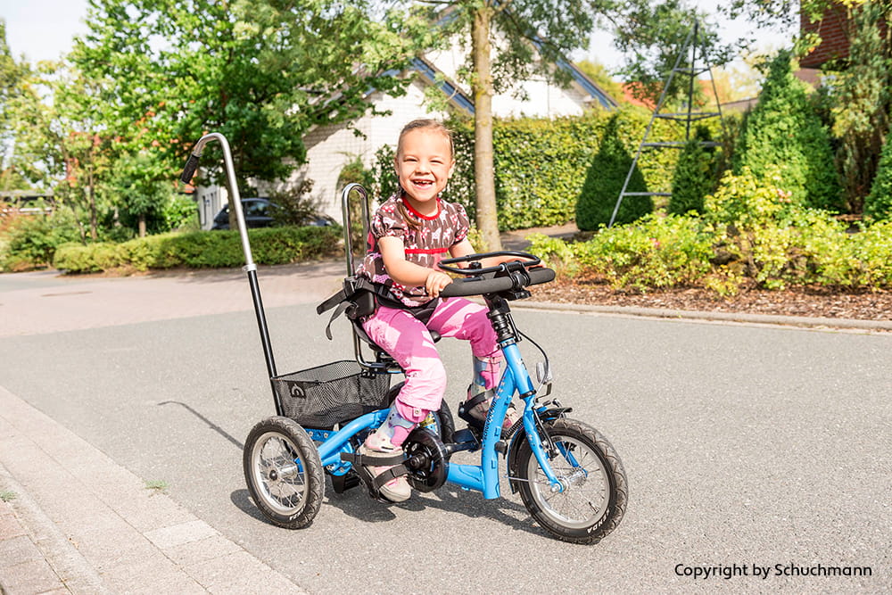 Lachendes Kind fährt mit einem angepassten Therapiedreirad auf einer ruhigen Straße