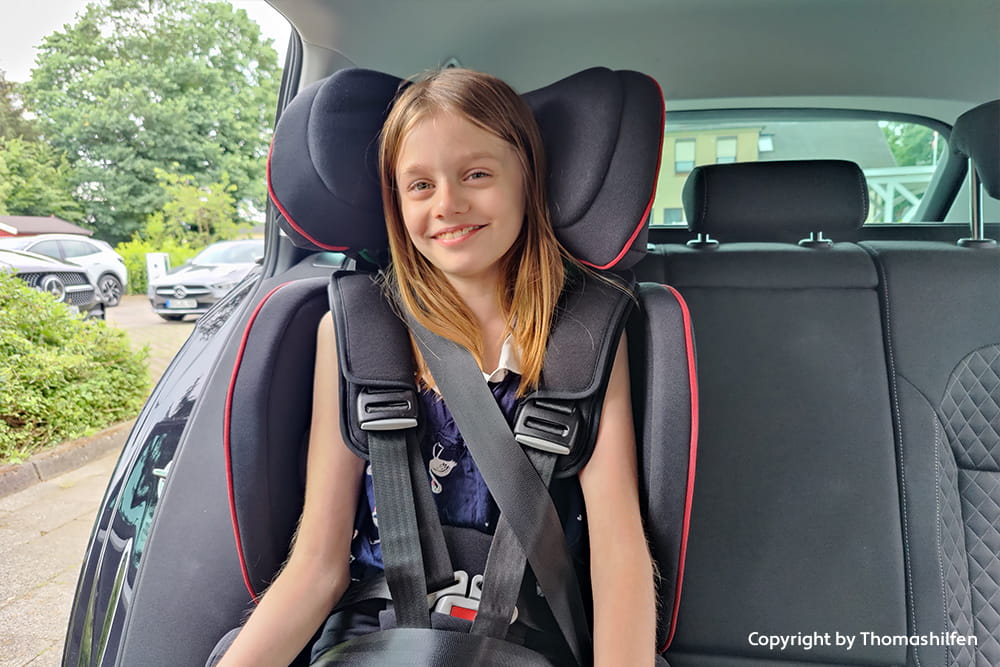 Mädchen sitzt angeschnallt in einem unterstützenden Auto-Kindersitz auf der Rückbank eines Autos