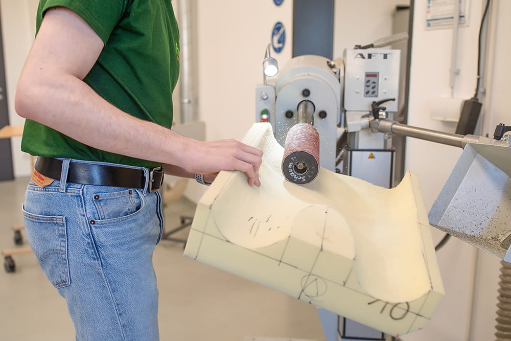 Mitarbeiter schleift ein individuell vorbereitetes Sitzkissen an einer Schleifmaschine in der Werkstatt