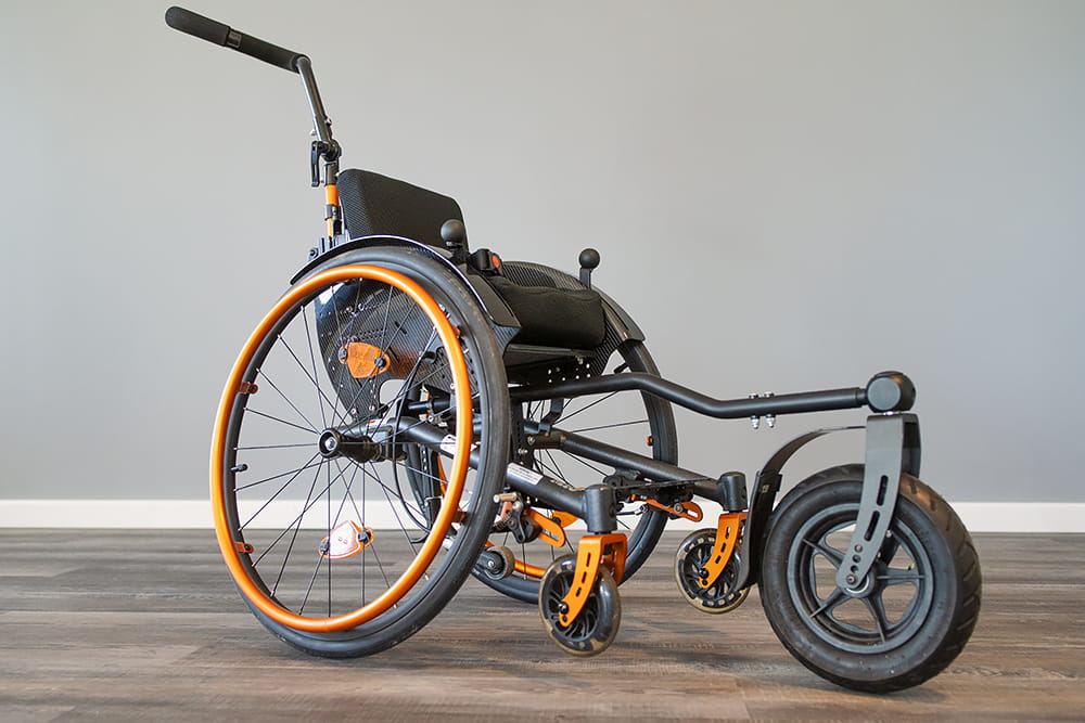 Sportlicher Rollstuhl mit orangefarbenen Details und großer Vorderradlösung auf hellem Hintergrund