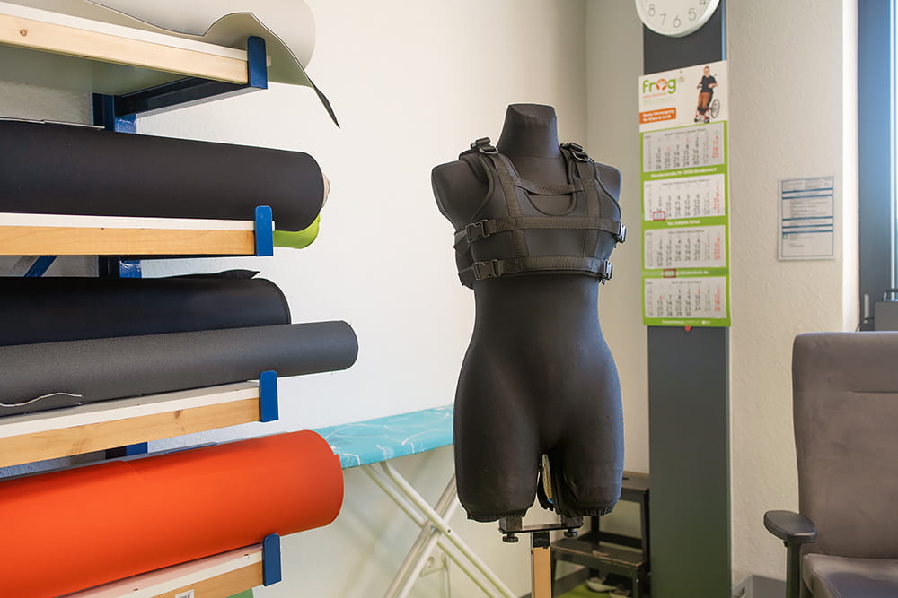 Schneiderpuppe mit Gurtsystem steht neben Stoffrollen und Arbeitsmaterialien in der Näherei