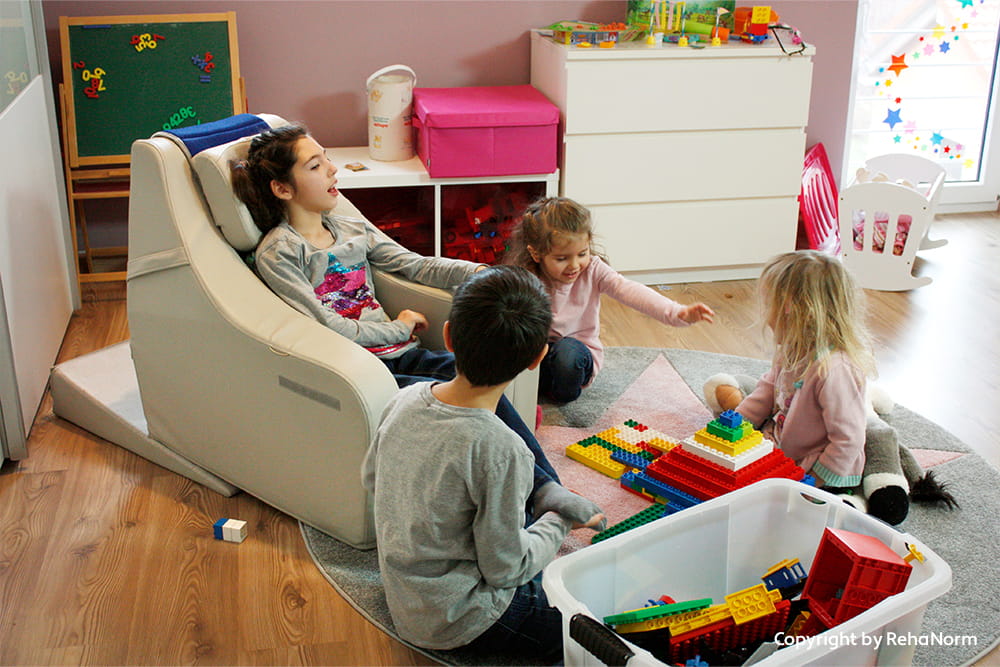 Kinder spielen gemeinsam mit Bauklötzen, während ein Kind in einer unterstützenden Sitzhilfe sitzt