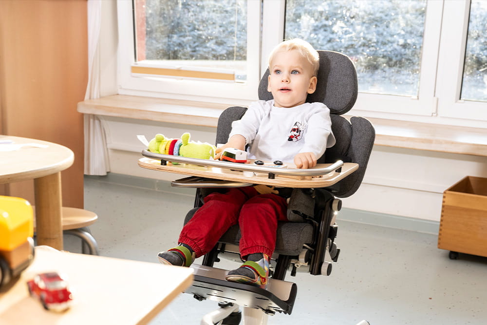 Ein Kind sitzt im Therapiestuhl und nutzt das Spielzeug vor sich.
