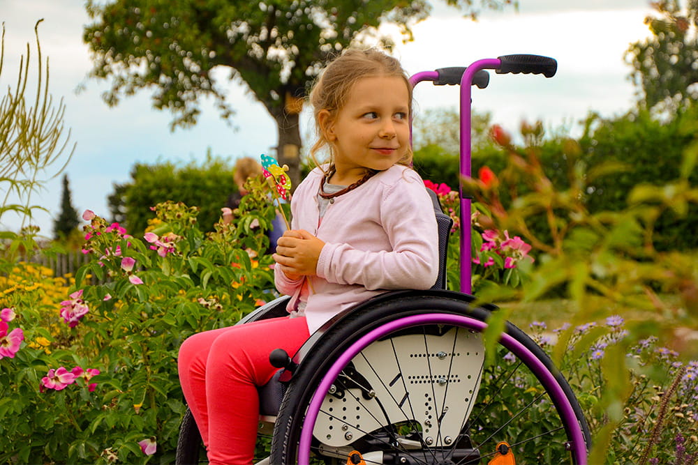 Mädchen sitzt im Rollstuhl und hält eine kleines Windrad in der Hand.