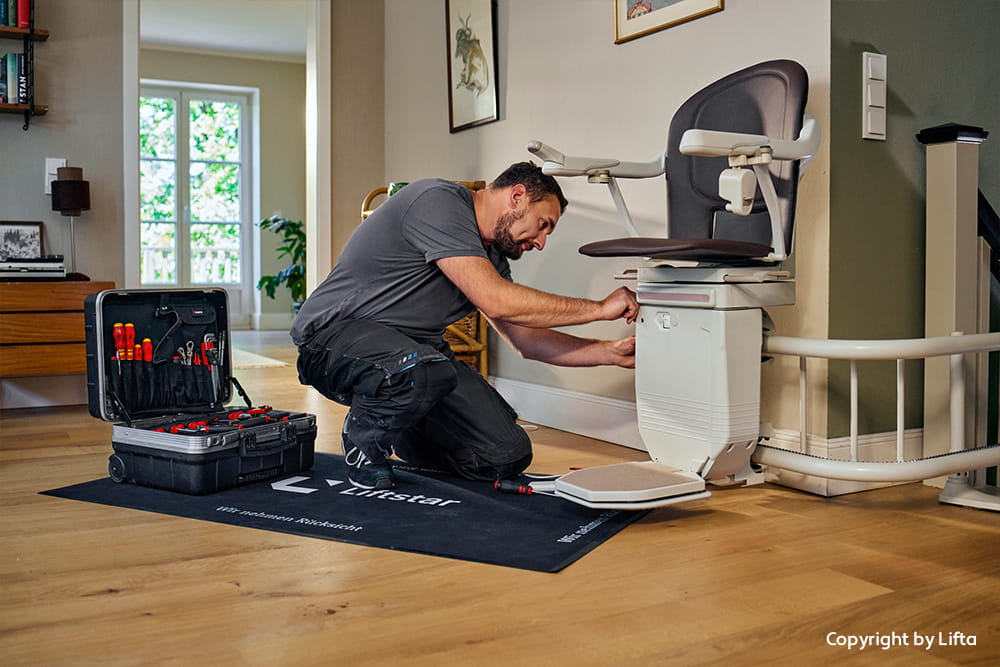Monteur arbeitet an einem Treppenlift im Wohnbereich und prüft die Befestigung an der Treppe