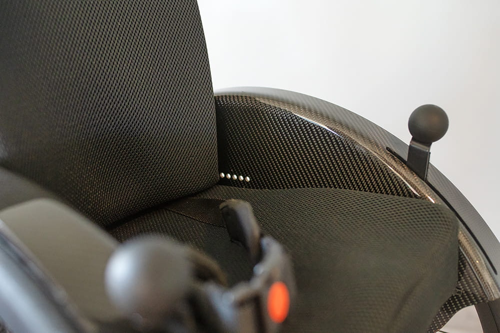 Detailaufnahme eines Rollstuhls mit Carbon-Seitenteil, Sitzfläche und Bedienelementen
