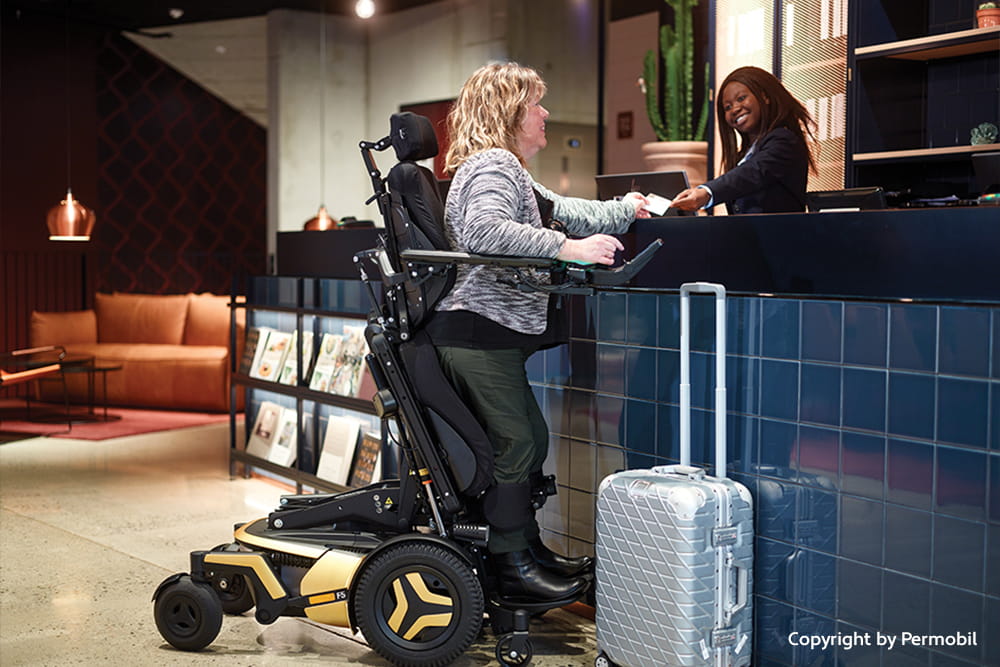 Person nutzt einen elektrischen Rollstuhl mit Standfunktion an einer Hotelrezeption