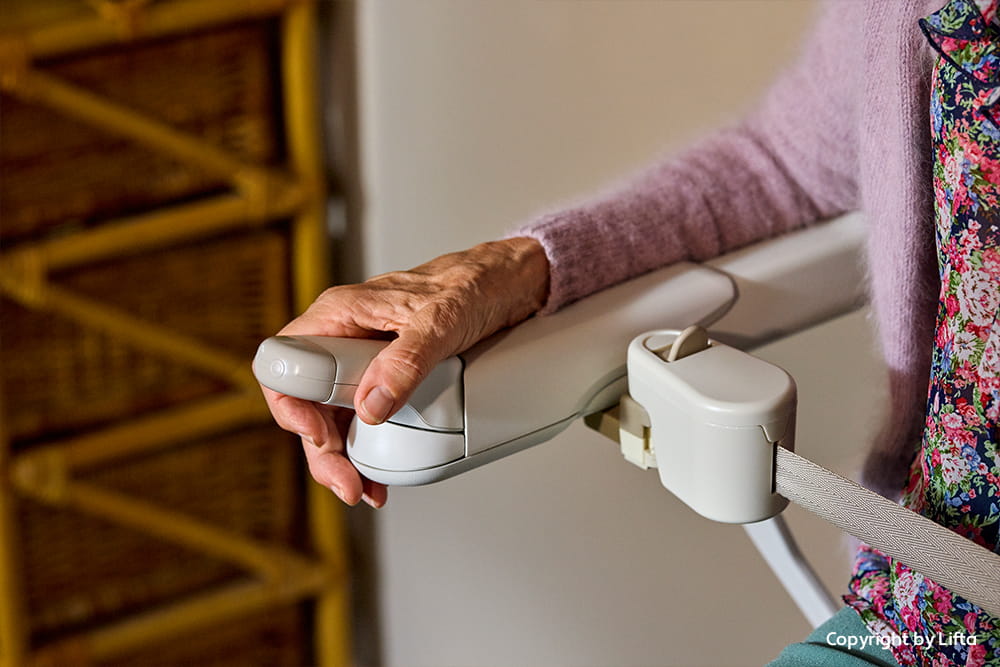 Frau sitzt auf einem Treppenlift und hat die Steuerung in der Hand