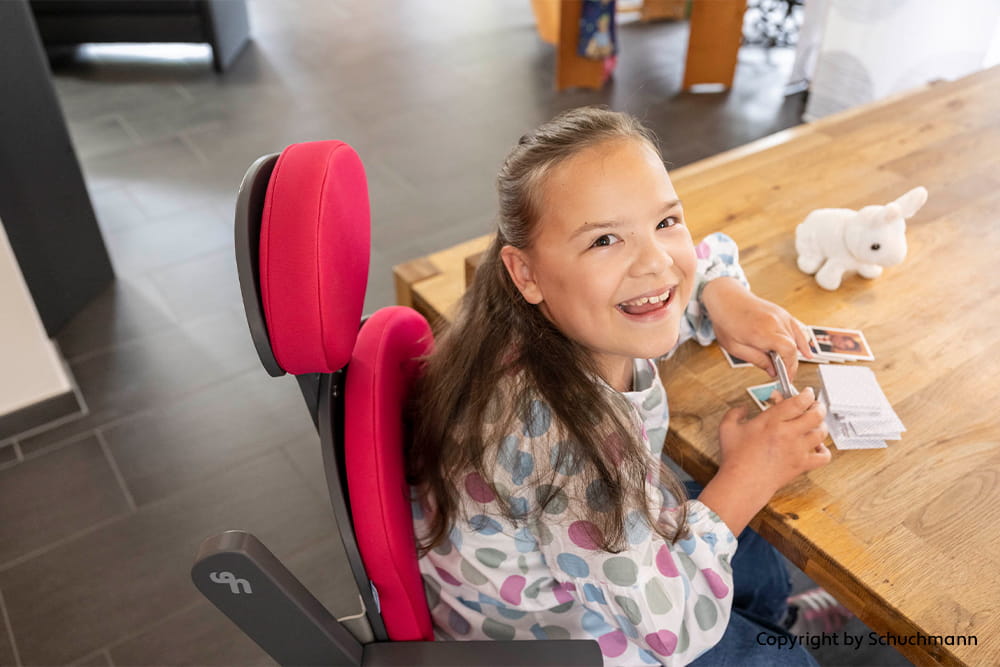 Ein Kind im Therapiestuhl spielt mit Karten am Esstisch